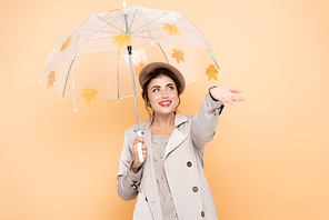 joyful woman with outstretched hand under umbrella, decorated with yellow leaves on peach