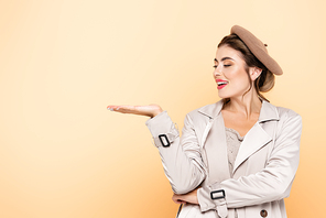 stylish woman in trench coat and beret pointing with hand on peach