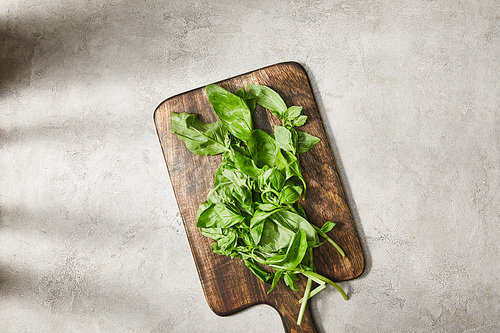 Top view of cutting board with basil leaves on grey