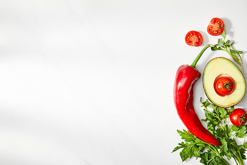 Top view of parsley, chili pepper, cherry tomatoes and avocado half on white background