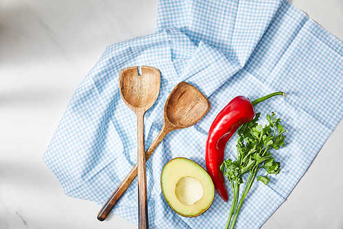 Top view of spatulas, parsley, chili pepper and avocado half on plaid cloth on white background