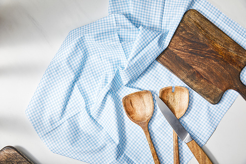 Top view of spatulas, knife and cutting board on plaid cloth on white background