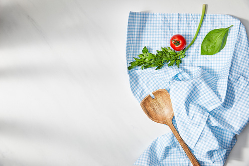 Top view of basil leaf, parsley, cherry tomato and spatula on plaid cloth on white background