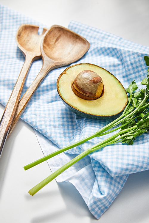 Selective focus of parsley, spatulas and avocado half on plaid cloth on white background