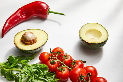 Cherry tomatoes, basil, chili pepper and avocado halves on white background