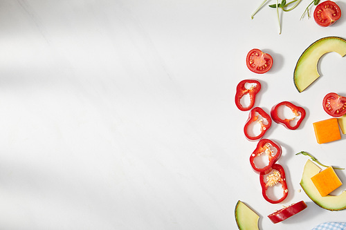 Top view of cut chili pepper, pumpkin and cherry tomatoes with avocado slices on white background