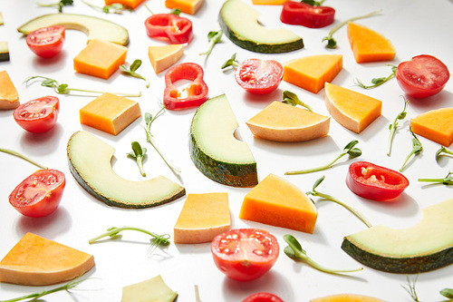 Selective focus of microgreens, cut ripe cherry tomatoes, chili pepper, pumpkin and avocado slices on white background