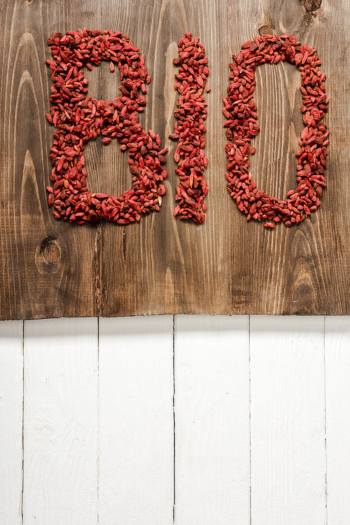 top view of word bio made of goji berries on cutting board on white wooden surface