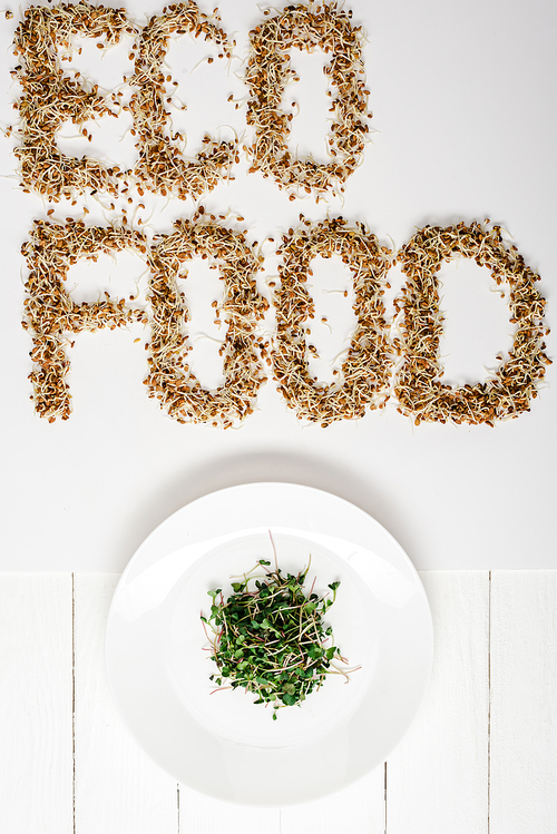top view of fresh microgreen on plate near  food lettering made of sprouts on white wooden surface