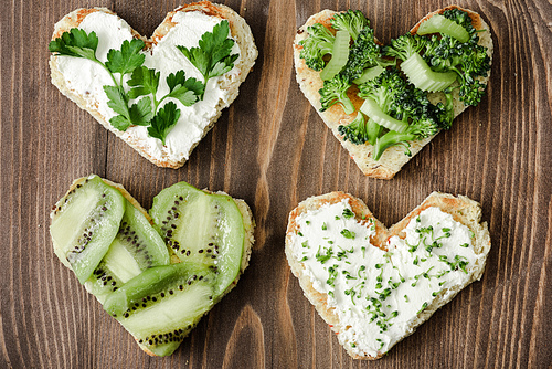 top view of heart shaped canape with creamy cheese, broccoli, microgreen, parsley and kiwi on wooden surface