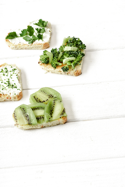 heart shaped canape with creamy cheese, broccoli, microgreen, parsley and kiwi on white wooden surface