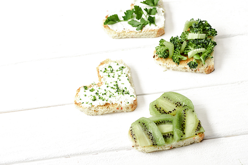 heart shaped canape with creamy cheese, broccoli, microgreen, parsley and kiwi on white wooden surface