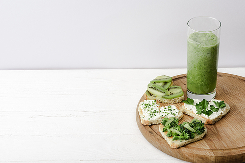 green smoothie and heart shaped canape with creamy cheese, broccoli, microgreen, parsley and kiwi on white wooden surface