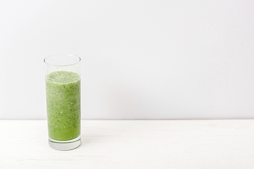green smoothie in glass on white wooden surface