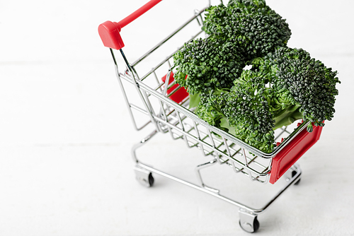 fresh green broccoli in shopping cart on white wooden surface