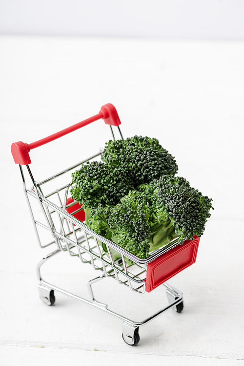 fresh green broccoli in shopping cart on white wooden surface