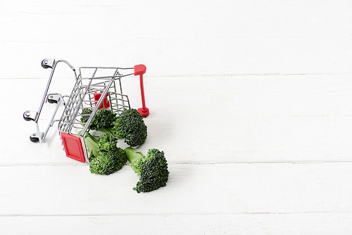 fresh green broccoli scattered from shopping cart on white wooden surface
