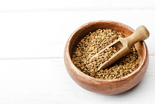 natural fenugreek in wooden bowl with spatula on white surface