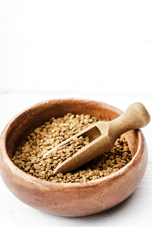 natural fenugreek in wooden bowl with spatula on white surface