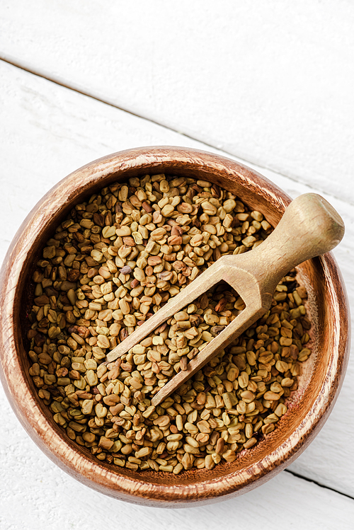 top view of natural fenugreek in wooden bowl with spatula on white surface