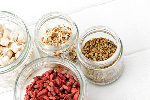 goji berries and sprouts in glass jars on white wooden surface