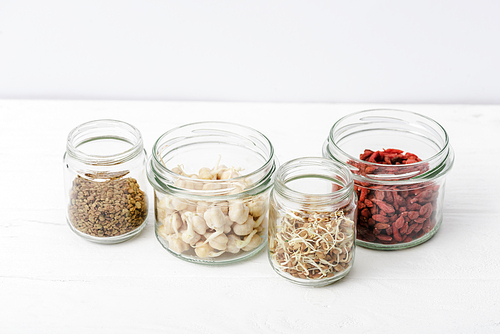 goji berries and sprouts in glass jars on white wooden surface