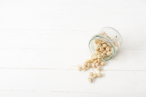 sprouts scattered from glass jar on white wooden surface