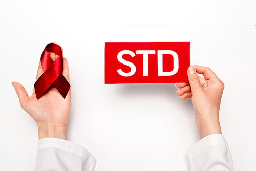 cropped view of doctor holding paper with std lettering and red ribbon on white