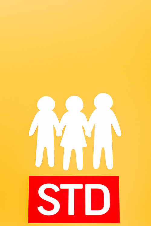 top view of three paper people near red paper with std lettering isolated on orange