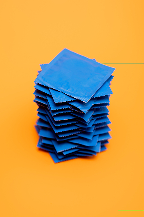stacked condoms in blue packs isolated on orange