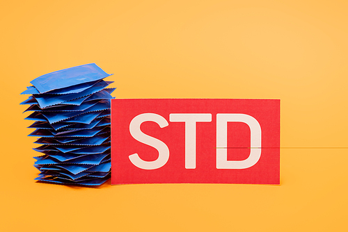 stack of condoms near paper with std lettering isolated on orange