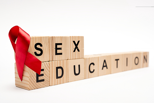 selective focus of wooden cubes with sex education lettering near red ribbon on white