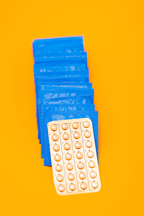 top view of contraceptive pills near packs with condoms isolated on orange
