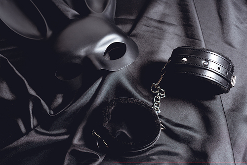rabbit mask near leather handcuffs on black silk fabric