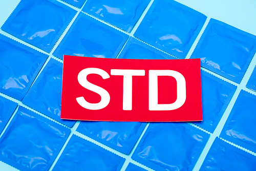 top view of red paper with std lettering on packs with condoms isolated on blue