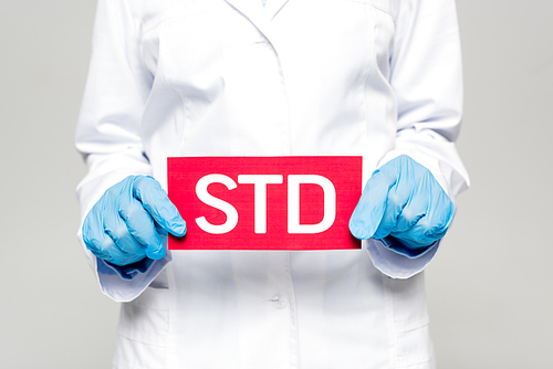 cropped view of doctor in blue latex gloves and white coat holding std lettering isolated on grey