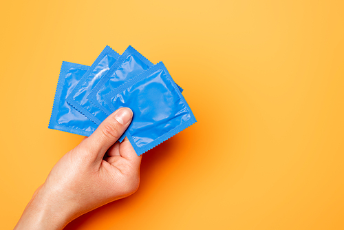 cropped view of woman holding blue packs with condoms on orange
