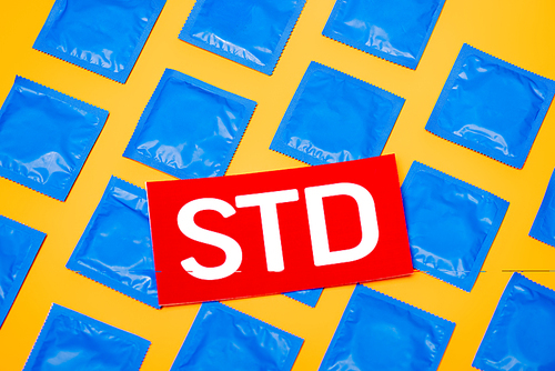 top view of paper with std lettering near blue packs with condoms isolated on orange
