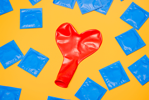 top view of red heart-shaped balloon near blue condoms isolated on orange