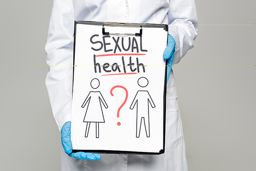 cropped view of doctor in blue latex gloves and white coat holding clipboard with sexual health lettering, drawn man and woman isolated on grey