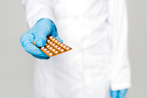 selective focus of doctor holding blister pack with contraceptive pills isolated on grey