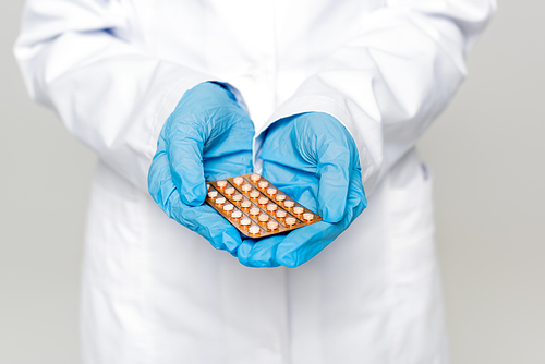 cropped view of doctor holding blister pack with contraceptive pills isolated on grey