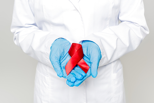 cropped view of doctor holding red ribbon isolated on grey