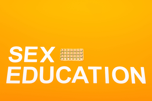 top view of sex education lettering near blister pack with contraceptive pills isolated on orange