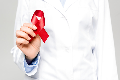 cropped view of doctor in white coat holding red ribbon isolated on grey