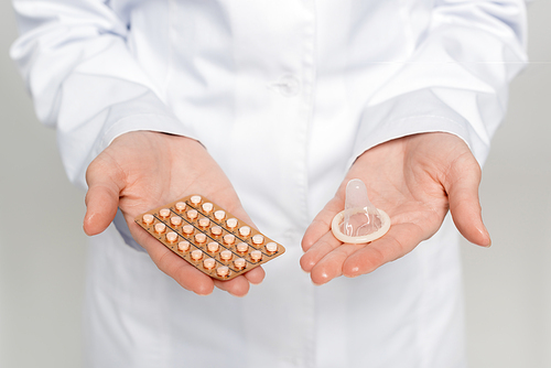 cropped view of doctor holding blister pack with contraceptive pills and condom isolated on grey