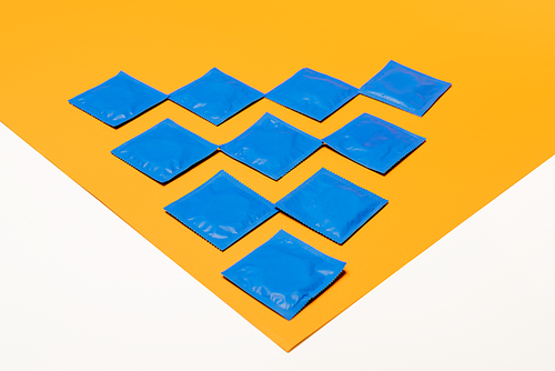 packs with condoms on orange surface isolated on white