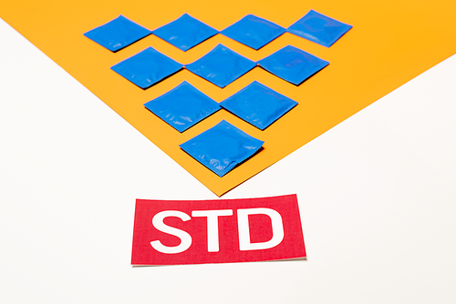 packs with condoms on orange surface near std lettering isolated on white