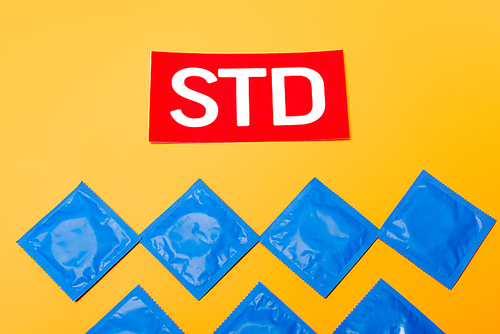 top view of packs with condoms near red std lettering isolated on orange