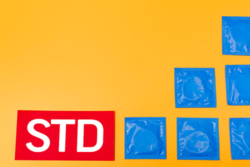 top view of packs with condoms near std lettering isolated on orange